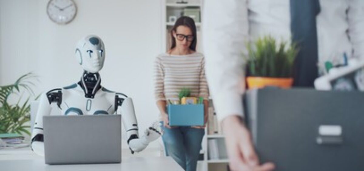 Robot working at a laptop while employees carry boxes out of an office.