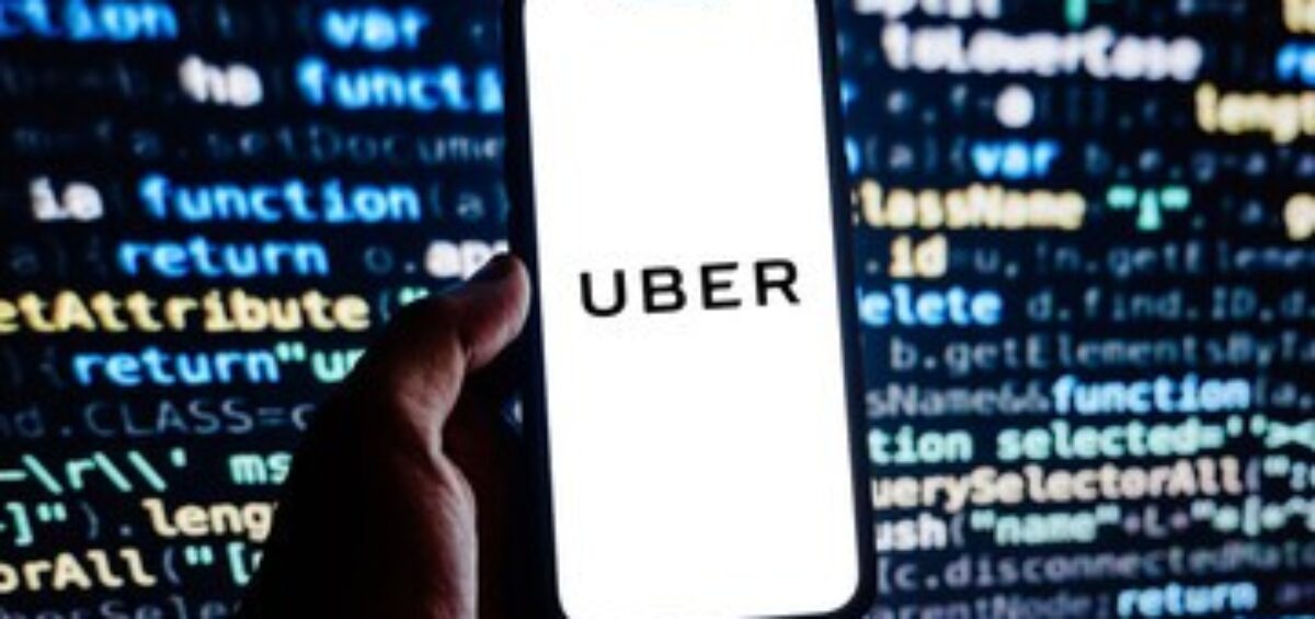 Hand holding a phone displaying Uber against a background of programming code.
