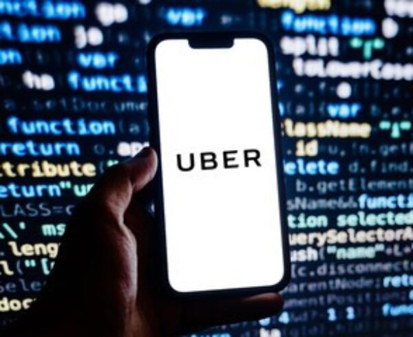Hand holding a phone displaying Uber against a background of programming code.